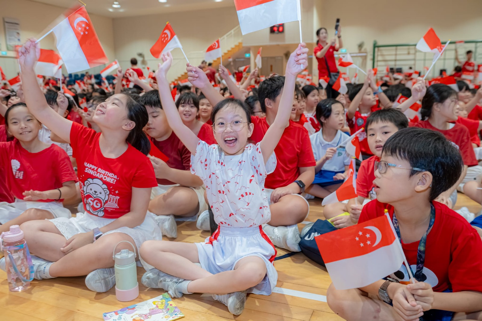 Pupils dressed in red and white waving energetically holding Singapore Flag!