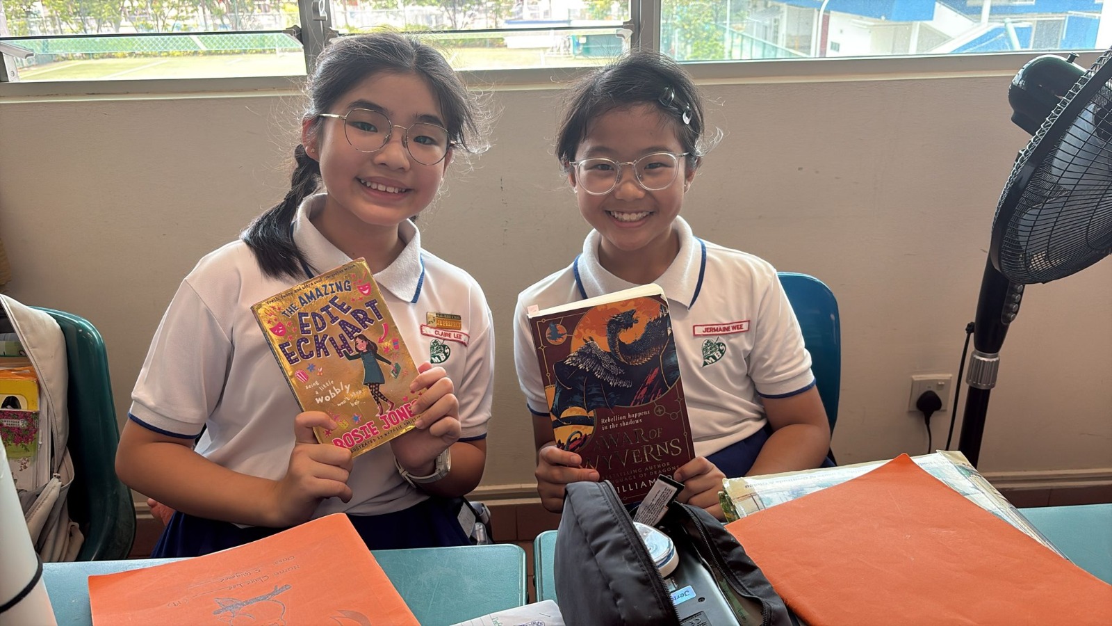 2 girls sitting in class dress in Maha Bodhi PE attire holding on to their favourite storybook