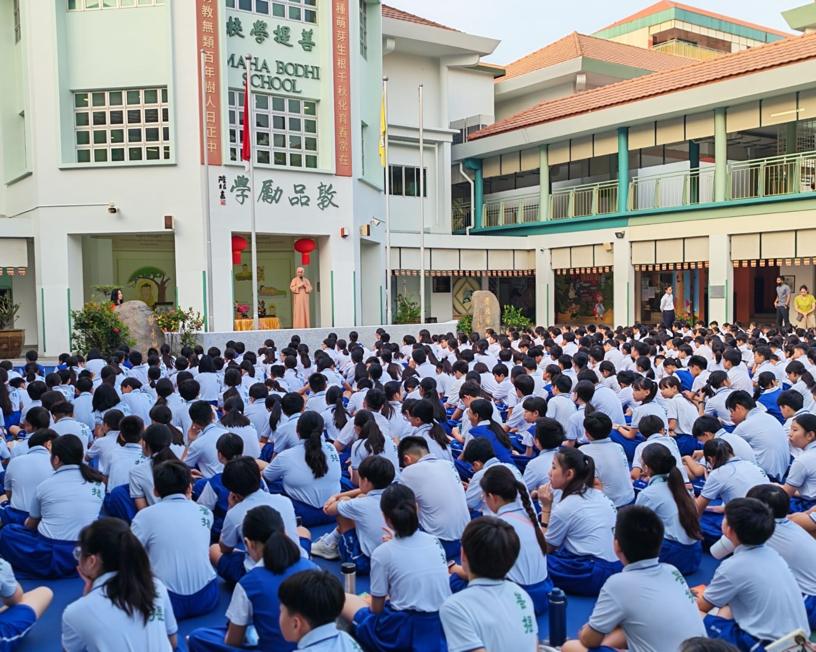 Pupils sitting in parade square under iconic clock tower listening to Venerable Seck Kwang Phing